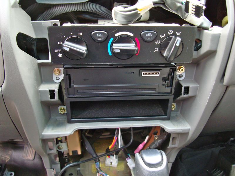 Car dashboard showing climate controls and a double-DIN stereo opening with wiring visible