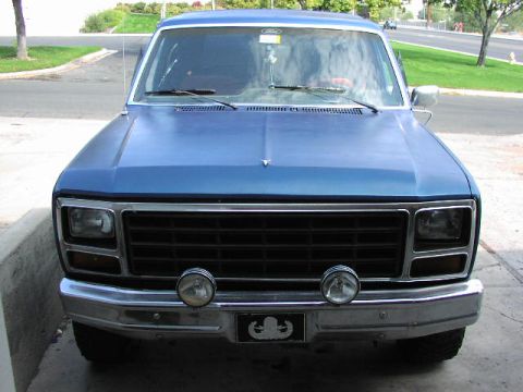 1981 Ford Bronco - This blue pickup truck is parked on a paved surface with a grassy area and street in the background.