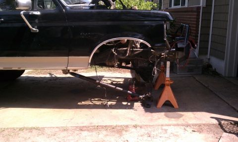 1990 Ford Bronco - Front end of a black Ford truck is disassembled and supported by jack stands.