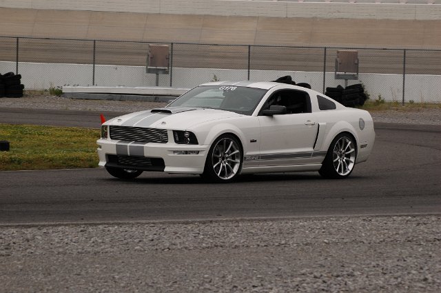 White 2007 Ford Mustang with gray racing stripes on a track