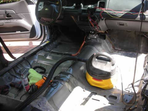 2004 Ford Crown Victoria - The interior of a 2004 Ford Crown Victoria is shown with the seats and carpeting removed, revealing the bare metal floor and various tools…