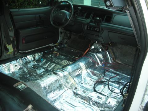 2004 Ford Crown Victoria - Interior of a 2004 Ford Crown Victoria undergoing sound deadening modifications, with the floor stripped and covered in insulation material.