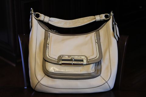 1999 Ford Crown Victoria - A cream-colored Coach handbag with textured accents and a prominent silver clasp is displayed against a dark background.