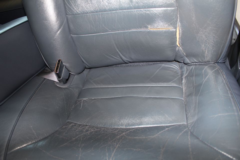 Worn gray leather car seat with cracked cushion and torn seatback exposing foam