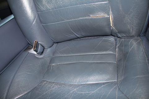 1999 Ford Crown Victoria - Interior view of a worn leather car seat with visible damage and a seatbelt.