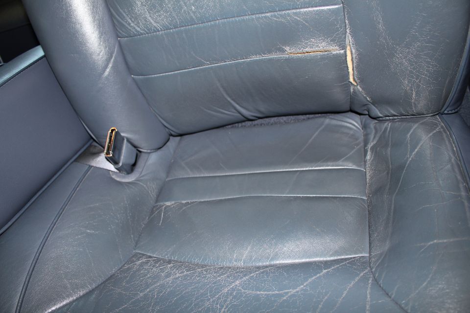 Close-up of a worn, gray leather car seat with a seatbelt buckle visible