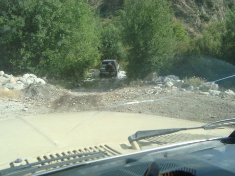 1986 Ford Bronco - Another vehicle navigates a water crossing on a dirt road surrounded by trees and rocky terrain.