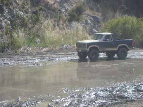 1986 Ford Bronco - This lifted 1980s Ford Bronco navigates a muddy trail, kicking up water as it goes.