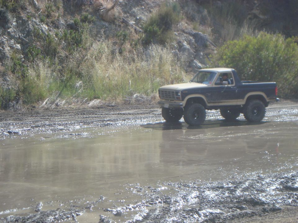 Tan and dark blue 1980s Ford Bronco driving through mud