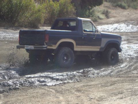 1986 Ford Bronco - This Ford Bronco is navigating a muddy off-road trail, demonstrating its off-road capabilities.