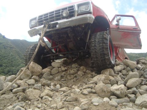 1986 Ford Bronco - This red off-road truck appears to be from the 1970s, not 1986, and is struggling on a rocky incline.