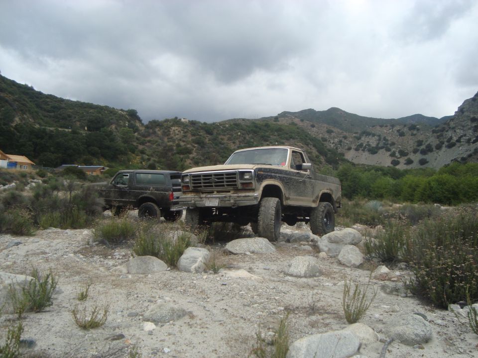 Ford pickup truck and Bronco parked on rocky terrain with mountains in background