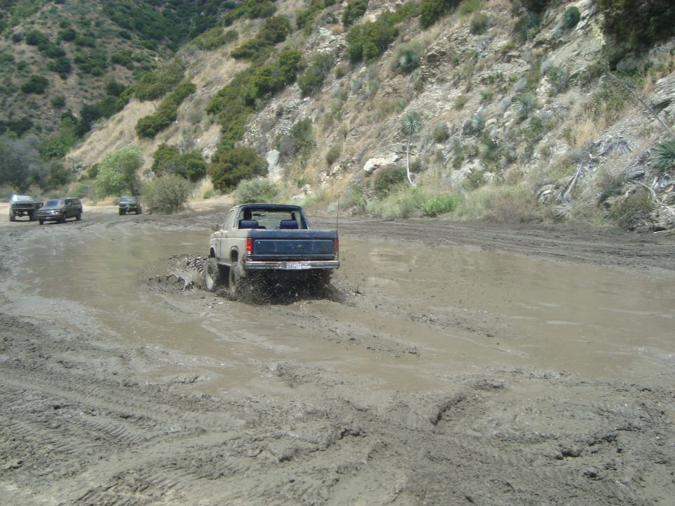 Bronco driving through mud pit with other SUVs behind it