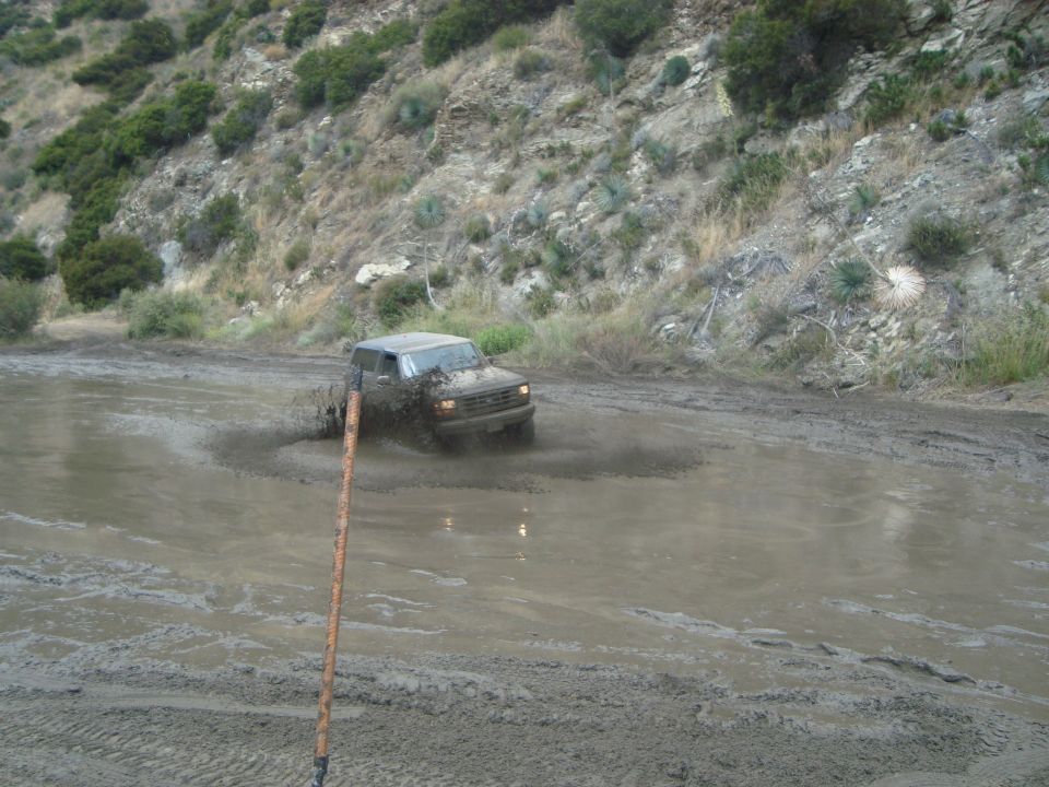 Mud-splattered dark SUV driving through a muddy puddle on a dirt road