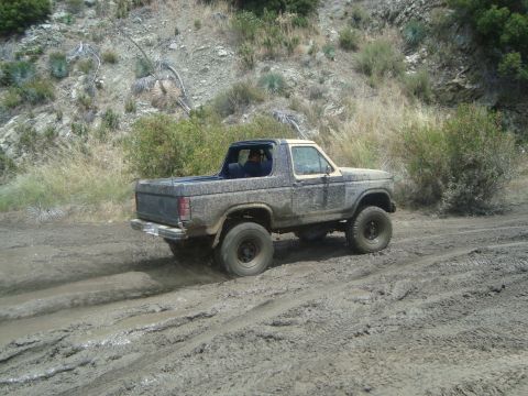 1986 Ford Bronco - This SUV is navigating a muddy trail, kicking up dirt and water as it goes.