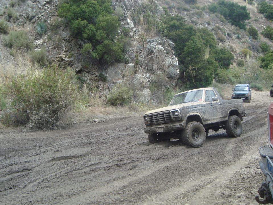Mud-covered 1980 Ford F-150 pickup truck with off-road tires driving on a dirt road