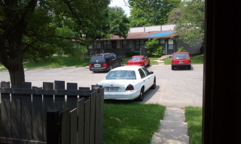 1998 Ford Crown Victoria - Distant rear three-quarter view of a white full-size Ford sedan with black steel wheels parked in an apartment lot, shot from a doorway pas…