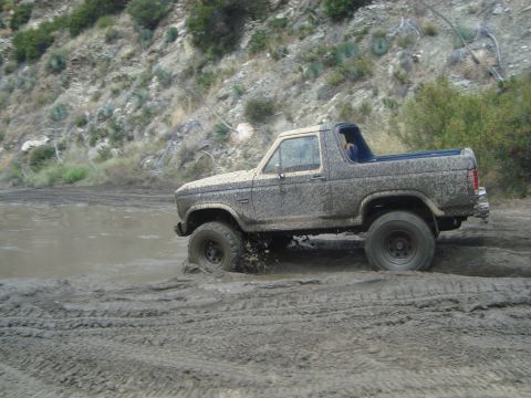 1986 Ford Bronco - This vehicle is covered in mud as it navigates a challenging off-road terrain.