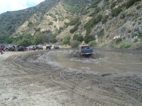 1986 Ford Bronco - Off-road vehicles navigate a muddy track in a scenic, hilly area.