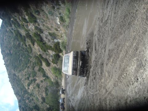 1986 Ford Bronco - Multiple vehicles navigate a challenging muddy terrain on a sunny day.