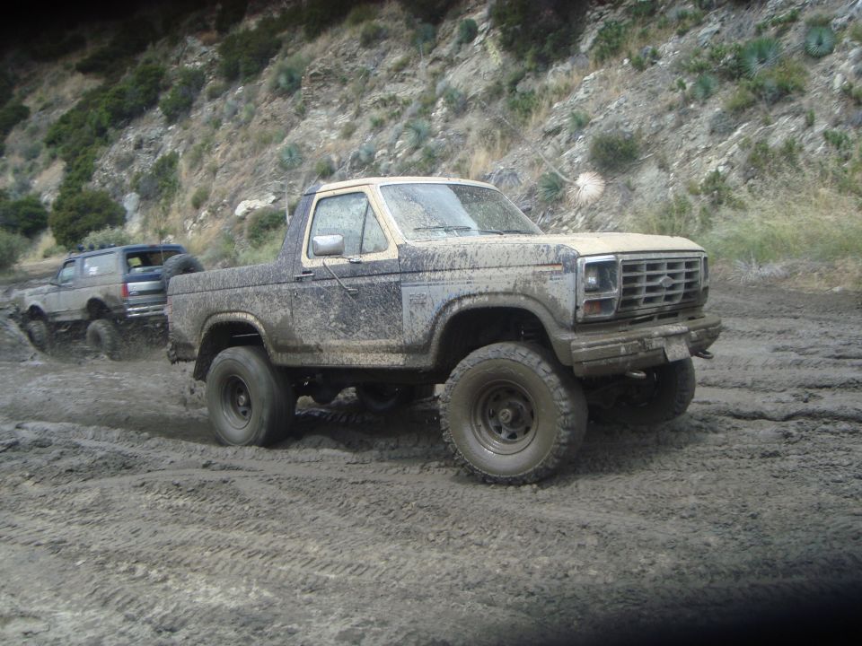 Mud-covered 1986 Ford Bronco driving through mud with another Bronco behind it