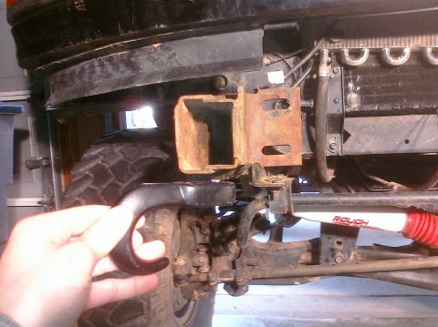 1995 Ford Bronco - A hand holds a black tow hook near the rusted front bumper bracket and tire of a vehicle.