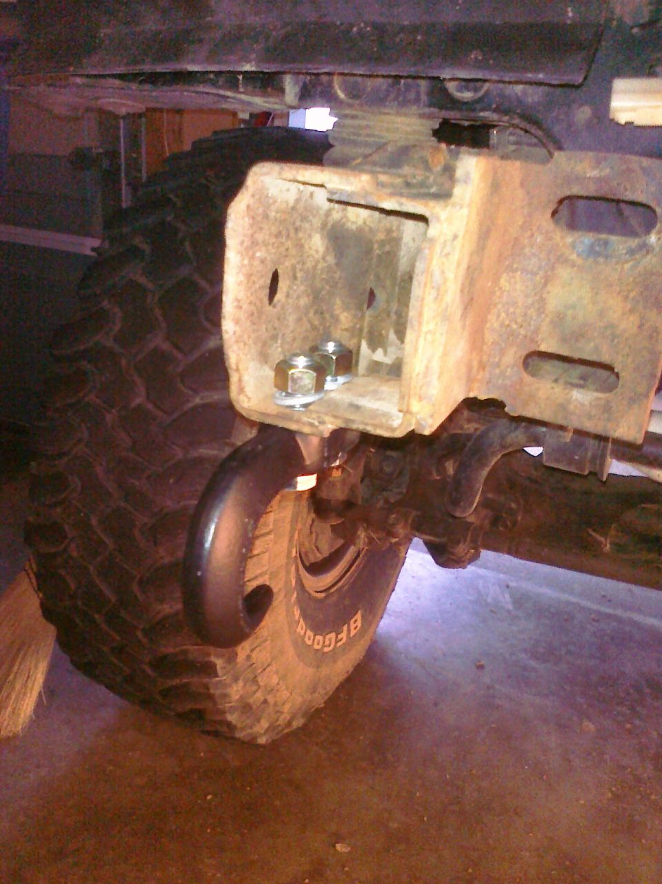 Close-up of a tow hook attached to a rusty bracket near a tire