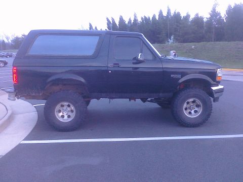 1995 Ford Bronco - Side view of a black Ford Bronco with aftermarket wheels and tires, parked in a lot.