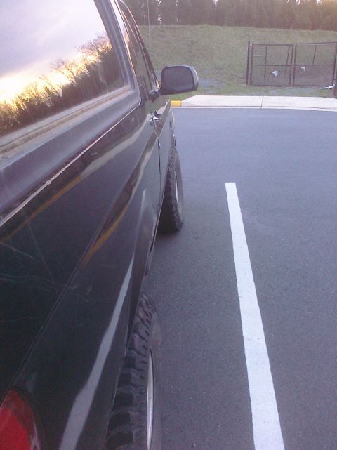 1995 Ford Bronco - Side view of a dark SUV parked in a lot, with a reflection of trees in the window.