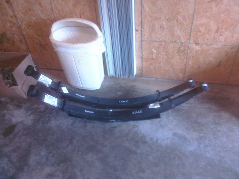 1995 Ford Bronco - Two new leaf springs are laid out on a concrete floor next to a white bucket and a cardboard box.