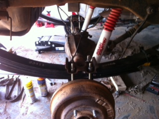 1995 Ford Bronco - Close-up of a vehicle's rear suspension components, including leaf springs and shocks, with another vehicle in the background.