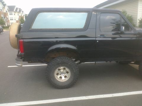 1995 Ford Bronco - Side profile of a black 1995 Ford Bronco parked in a lot, showing its spare tire.