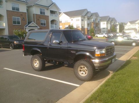 1995 Ford Bronco - A black 1995 Ford Bronco is parked in a lot next to apartment buildings.