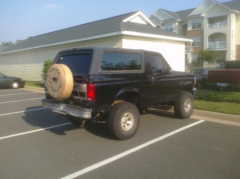 1995 Ford Bronco - This black Ford Bronco is parked in a lot with apartment buildings in the background.