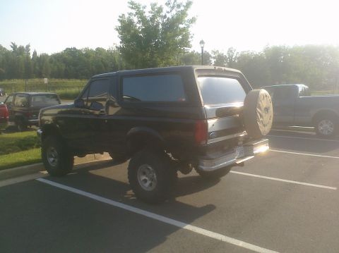 1995 Ford Bronco - A lifted black Ford Bronco is parked in a lot next to another vehicle.