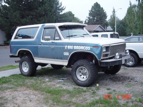 1989 Ford Bronco - A lifted blue and white Ford Bronco is parked on grass with another vehicle in the background.