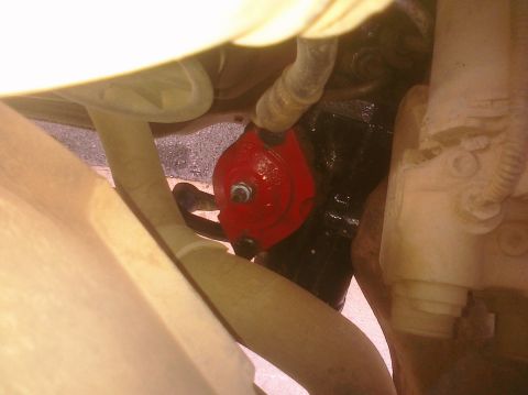 1995 Ford Bronco - A close-up, low-angle view of a red component, possibly a steering component, attached to a black mechanical part on the underside of a veh…