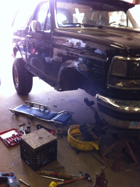 1993 Ford Bronco - A black Ford Bronco is undergoing maintenance in a garage, with tools and equipment scattered around.