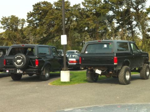 1993 Ford Bronco - Two black Ford Broncos are parked side-by-side, one with a spare tire mounted on the back.