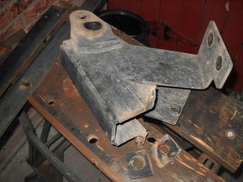 1986 Ford Bronco II - A metal bracket part is shown resting on a wooden workbench, with other metal pieces and a black bucket in the background.