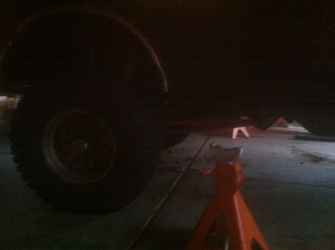1990 Ford Bronco - Dimly lit garage shot of a vehicle's rear wheel and tire supported on an orange jack stand over a concrete floor.