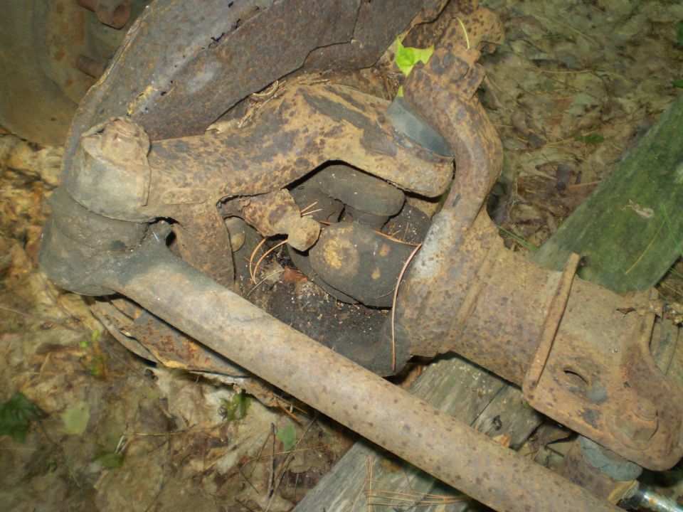 rusted vehicle axle components, including tie rod ends and steering knuckle parts, lying on the ground