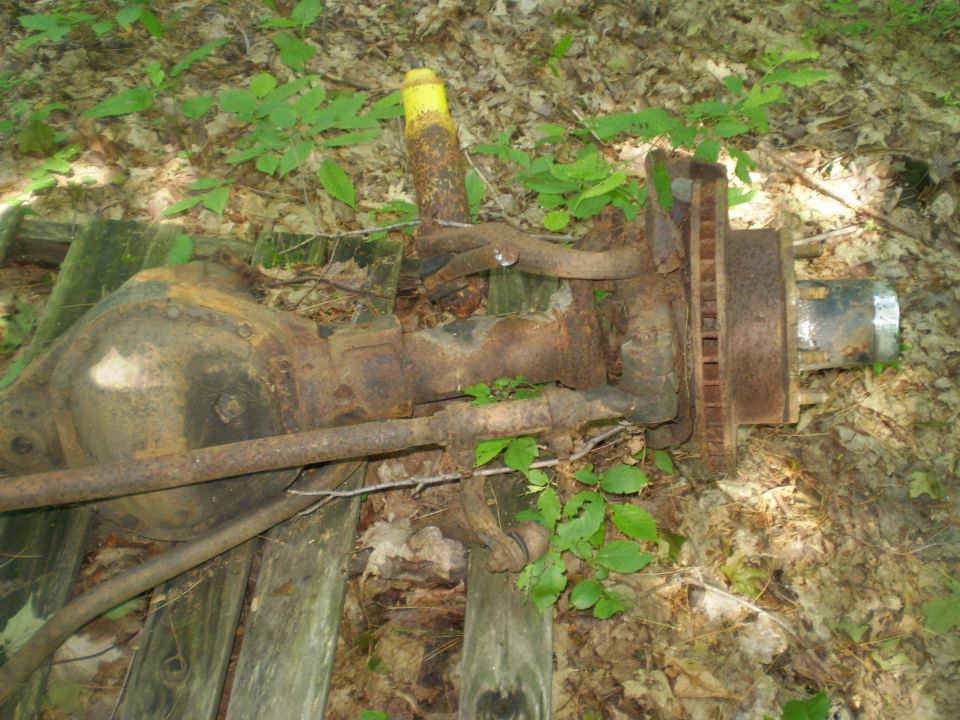 rusty axle assembly with shock absorber and brake rotor, sitting on wooden planks in woods