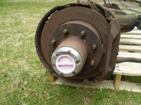 1979 Ford Bronco - A heavily rusted front axle assembly, identified by a Ford hub, sits on a pallet outdoors.