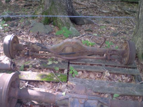 1979 Ford Bronco - This rusty rear axle assembly, likely from an older vehicle, is shown resting on wooden pallets in an outdoor setting.