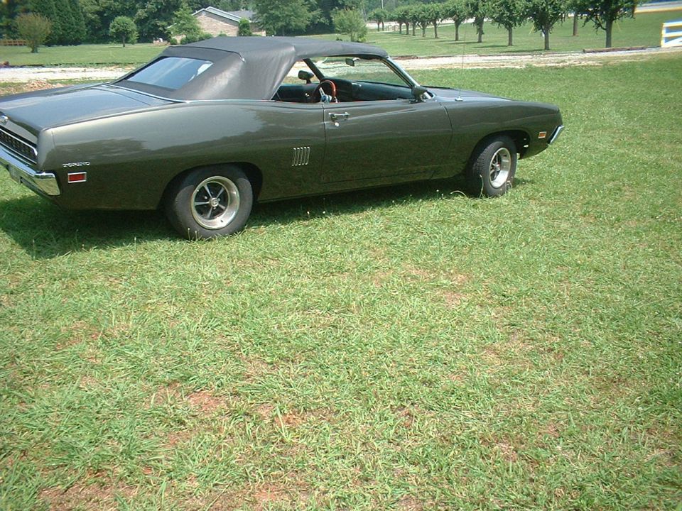 Green 1970 Ford Torino convertible parked on grass. It has a black soft top and chrome wheels