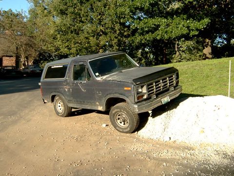 1982 Ford Bronco - A dark gray Ford Bronco is parked on a gravel surface with its front right tire elevated on a pile of white stones.