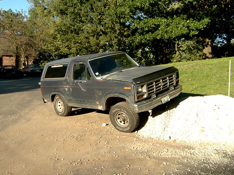 Dark gray Ford Bronco parked on gravel, front right tire on a pile of white stones. The grille has horizontal bars