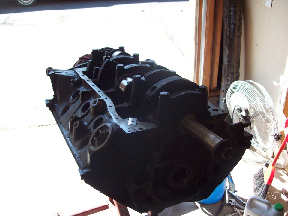 Engine block with crankshaft installed, resting on a stand. A fan is visible in the background