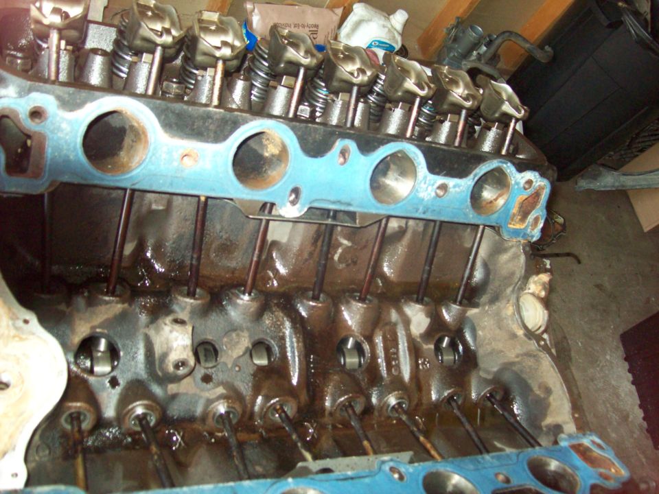 Engine block with blue gasket and pushrods, showing internal components and oil residue